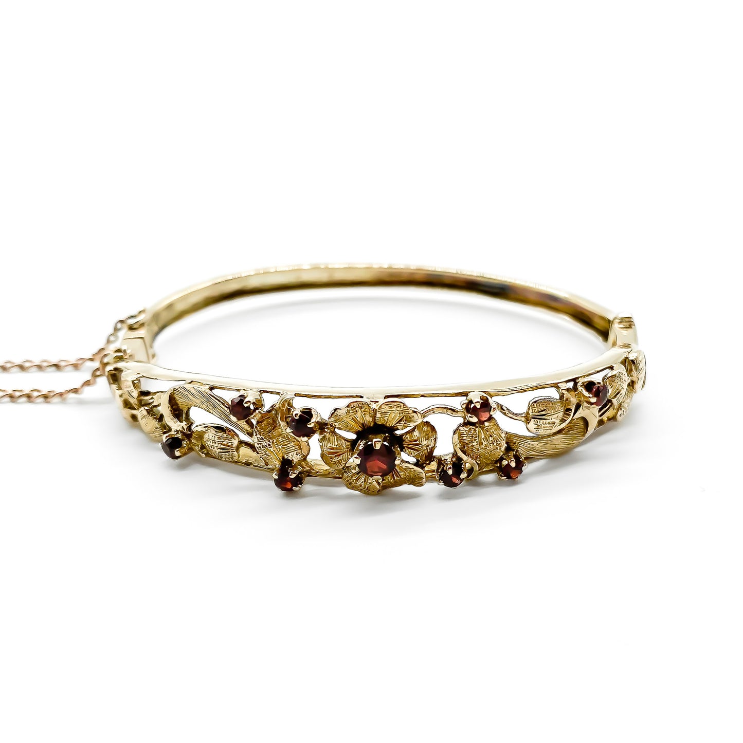 Beautiful 9ct rose gold bangle set with nine faceted garnets in a lovely floral design. Gold safety chain attached.