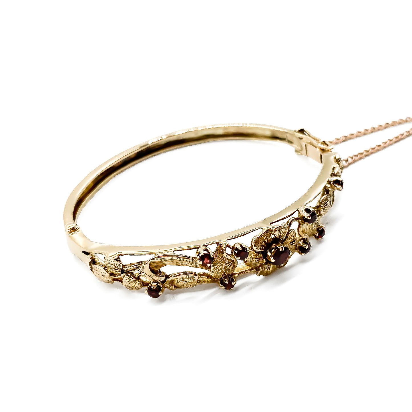Beautiful 9ct rose gold bangle set with nine faceted garnets in a lovely floral design. Gold safety chain attached.