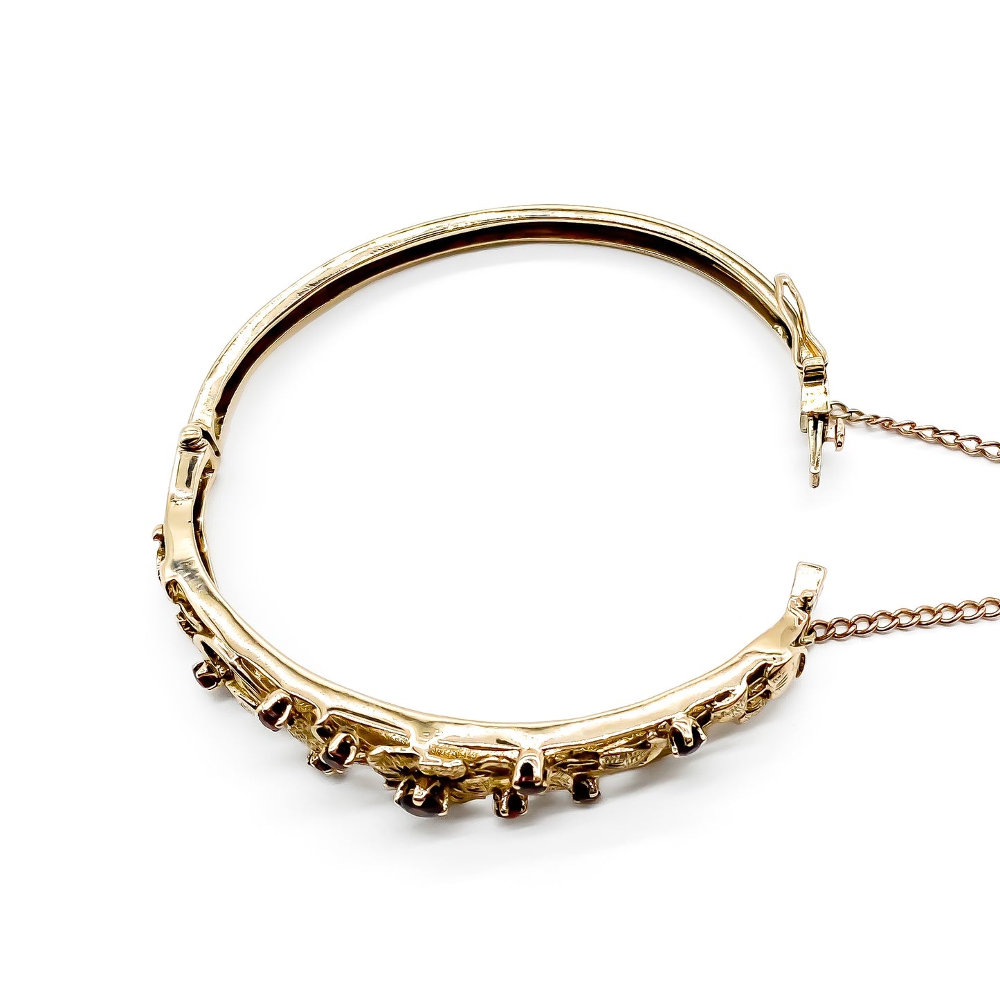 Beautiful 9ct rose gold bangle set with nine faceted garnets in a lovely floral design. Gold safety chain attached.