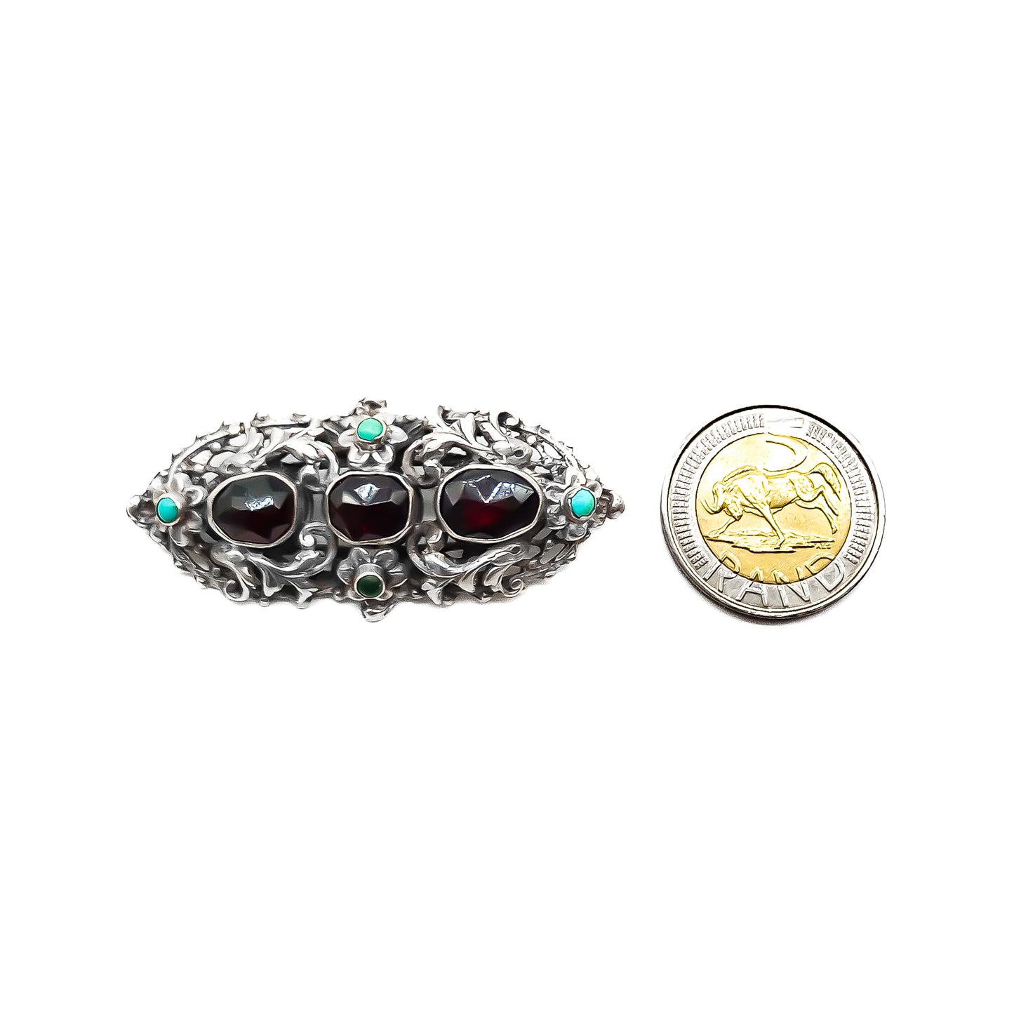 Intricate sterling silver Arts and Crafts brooch set with three large faceted Bohemian garnets and four small turquoise stones. Zoltan White & Company.
