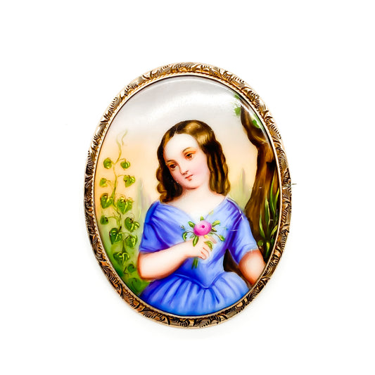 Charming Victorian hand painted porcelain brooch depicting a young girl holding a flower in a rose gold plated frame.