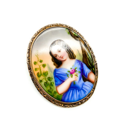 Charming Victorian hand painted porcelain brooch depicting a young girl holding a flower in a rose gold plated frame.