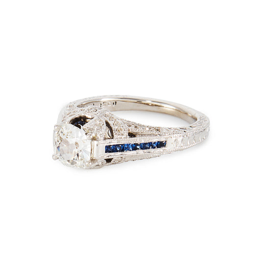Magnificent 14ct white gold ring, set with a 0.70ct Old-European-Cut diamond, as well as seven princess-cut sapphires on each shoulder. The ring also features a diamond encrusted gallery. A valuation from The Gem Lab is included.