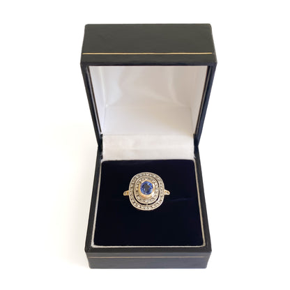 Beautiful Art Deco 14ct white and yellow gold ring set with an oval cornflower blue sapphire surrounded by two rows of small diamonds, as well as a small diamond on each shoulder. Italy