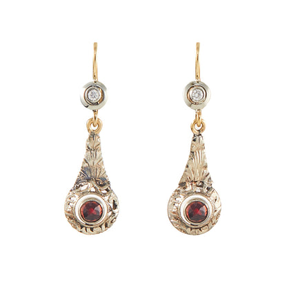 A pair of gold and silver drop earrings with a small clear stone at the top and a round red gemstone at the bottom, shown on a plain white background.