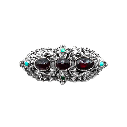 Intricate sterling silver Arts and Crafts brooch set with three large faceted Bohemian garnets and four small turquoise stones. Zoltan White & Company.